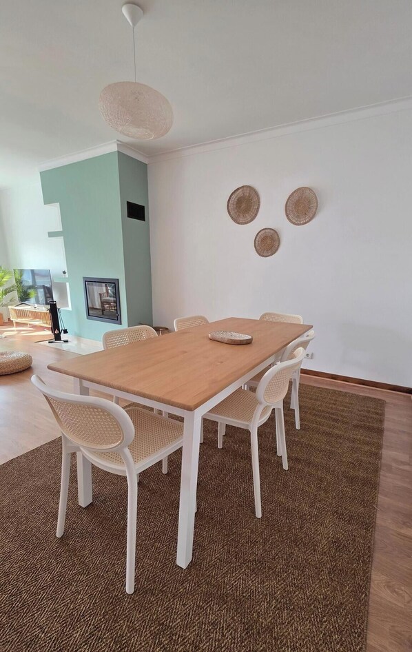A dining area with a wooden table and white chairs, a woven rug, and wall-mounted decorative plates.