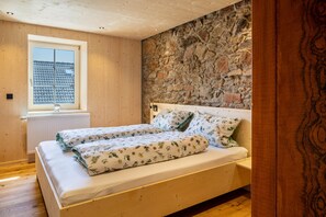 Ein Schlafzimmer mit einer Steinwand, Holzboden und einem Fenster mit Blick auf Gebäude.