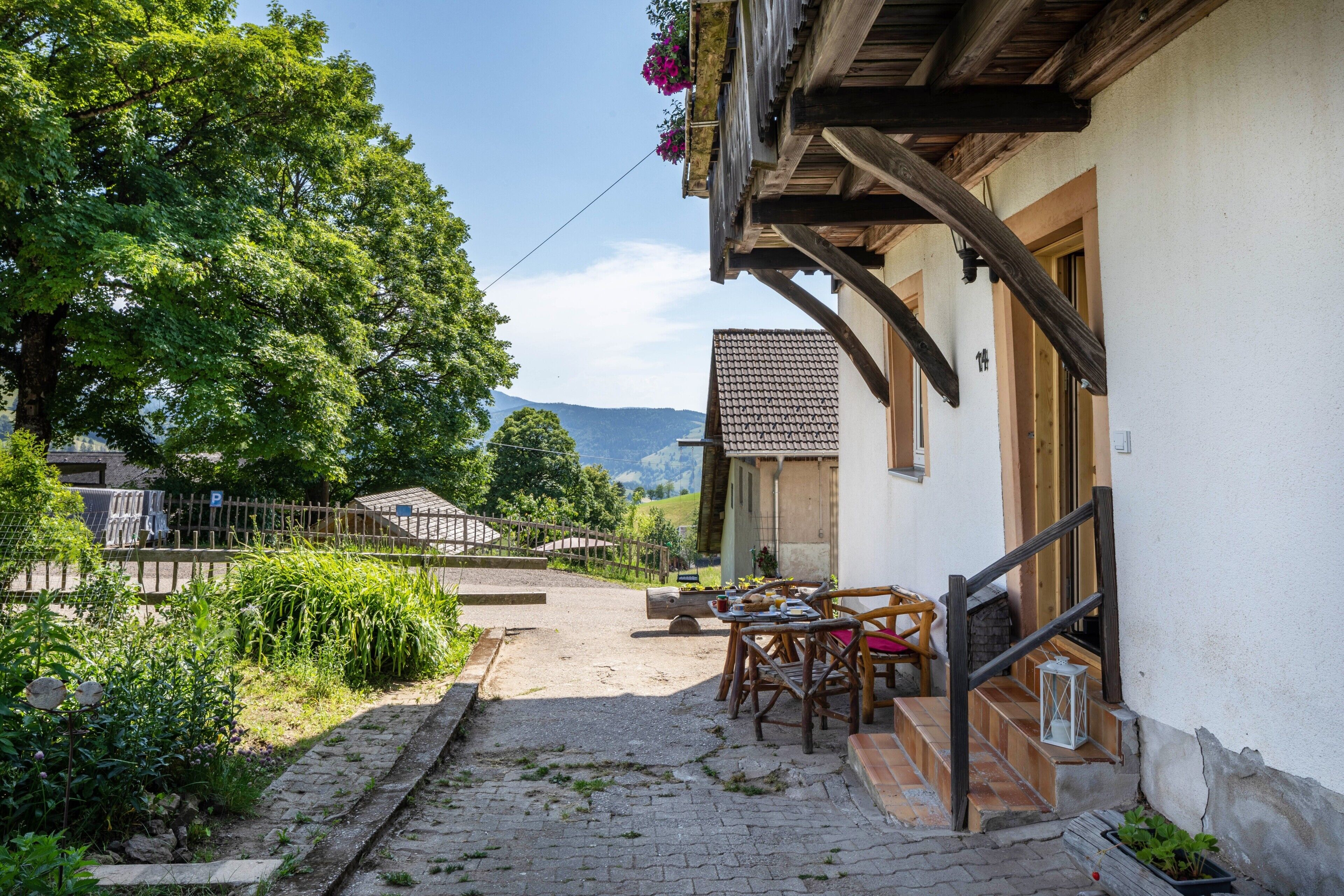 Un patio con una mesa y sillas de madera, un sendero de piedra y un edificio con tejado de baldosas.