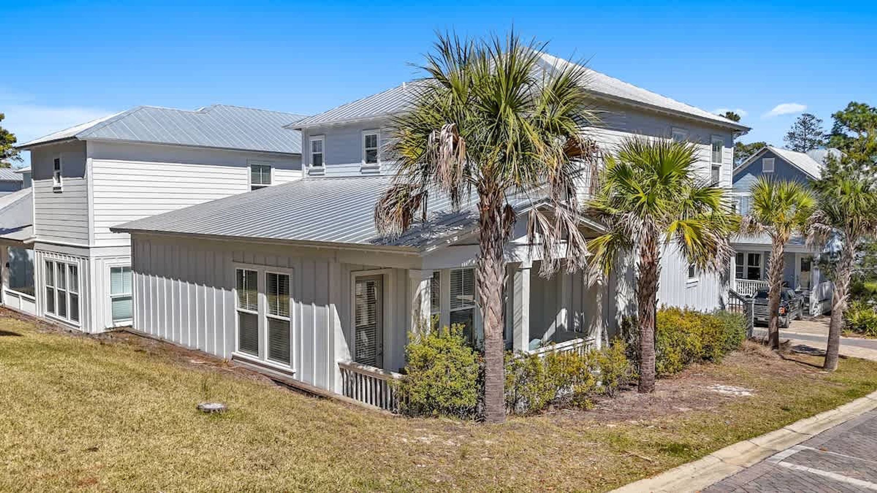 A two-story residential building with a gabled roof, a front porch, and a small front yard with palm trees and shrubs.