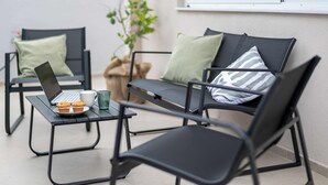 A modern outdoor seating area with two black chairs, a table with a laptop, a cup, and muffins.