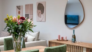 A dining area with a table, chairs, a vase with flowers, a mirror, and wall art.