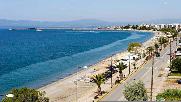 A coastal road with beachside views, a marina, and buildings along the shore.