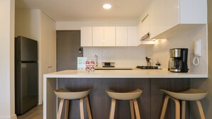 Een moderne keuken met een centraal eiland, barkrukken, een koffiezetapparaat en een koelkast.