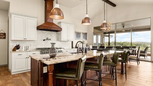Een moderne keuken met witte kasten, een groot eiland en hangende lampen.