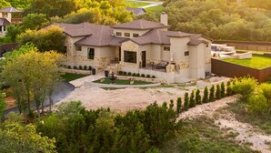 A large house with a stone facade, multiple chimneys, and a well-maintained lawn. - Luxury Hilltop Villa- Sunsets/Pool&HotTub/Game Rm/Gym/SteamRm/Sauna/Sleeps16 (New Braunfels)