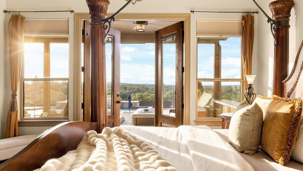 Een slaapkamer met een groot bed, uitzicht op de omgeving en een balkon.