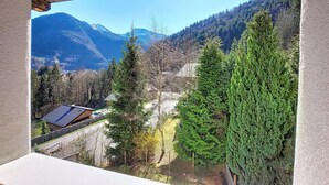 Vista de montanha a partir de um quarto com teto de madeira, janela com vista para uma estrada com casas e uma cordilheira ao longe.