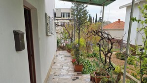 Un passadís cobert amb plantes en testos, terra de rajola i entrada d'un edifici.