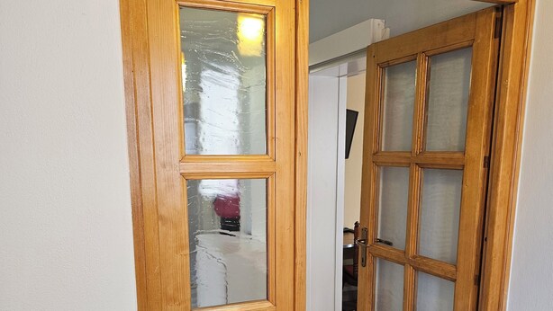 Una porta de fusta amb un panell de vidre i una porta més petita a la dreta.