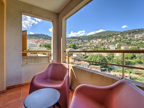 Ein Balkon mit zwei Stühlen und einem kleinen Tisch, mit Blick auf eine Stadtlandschaft aus Gebäuden und Hügeln.