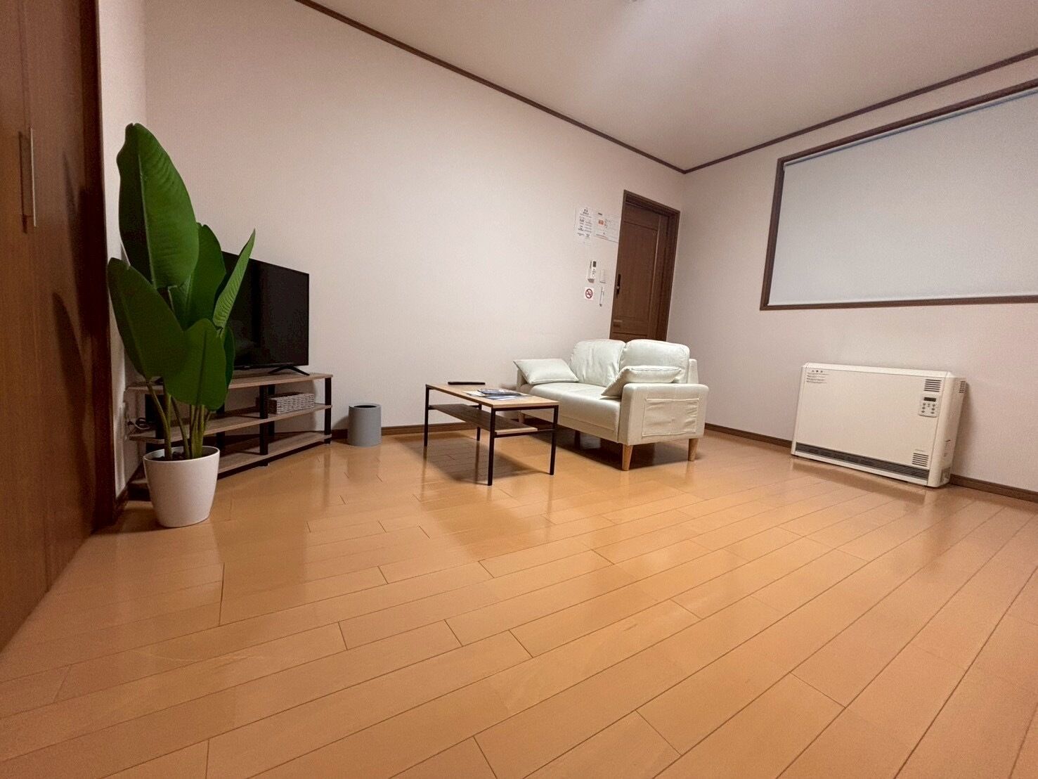 Un salón con sofá, mesa de centro, televisor, radiador y planta en maceta.
