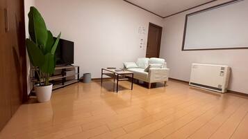 Un salón con sofá, mesa de centro, televisor, radiador y planta en maceta.
