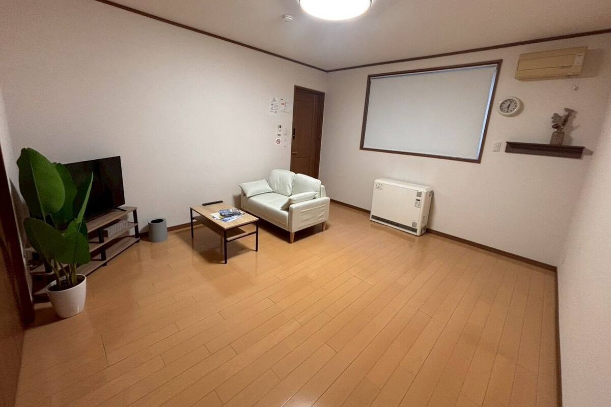 Una sala de estar con un sofá, una mesa de centro, un televisor, una planta y una pizarra en la pared.