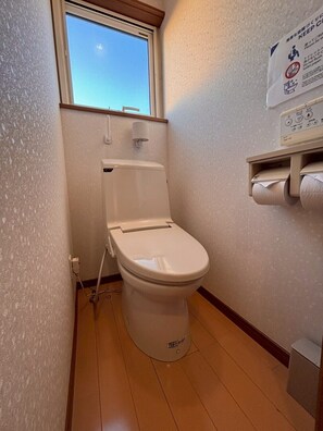 Un baño pequeño con inodoro, ventana y porta rollos.