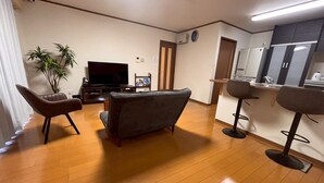 A living room with a flat-screen TV, a sofa, a chair, a small table, and a potted plant. - YORIDOKORO (Oma)