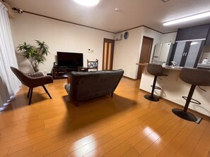 A living room with a flat-screen TV, a sofa, a chair, a small table, and a potted plant. - YORIDOKORO (Oma)