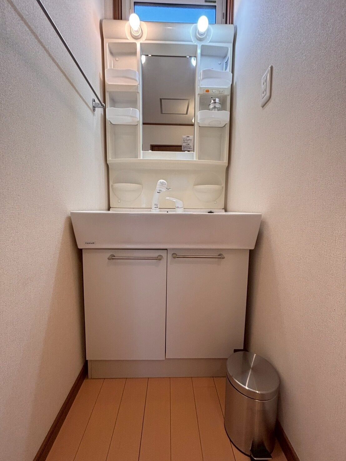 A small bathroom with a white sink, mirror, and a trash bin.