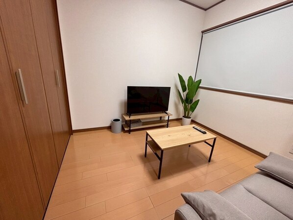 A room with a wooden floor, a TV on a stand, a small table, a potted plant, and a whiteboard on the wall. - YORIDOKORO (Oma)