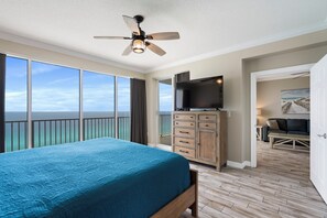 A bedroom with a large bed, a ceiling fan, a TV, and a view of the ocean. - Gulf Views & Family Fun – 3BR Boardwalk Condo (Panama City Beach)