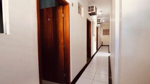 Un pasillo con puerta de madera, paredes blancas, suelo de baldosas y un ventilador de techo.