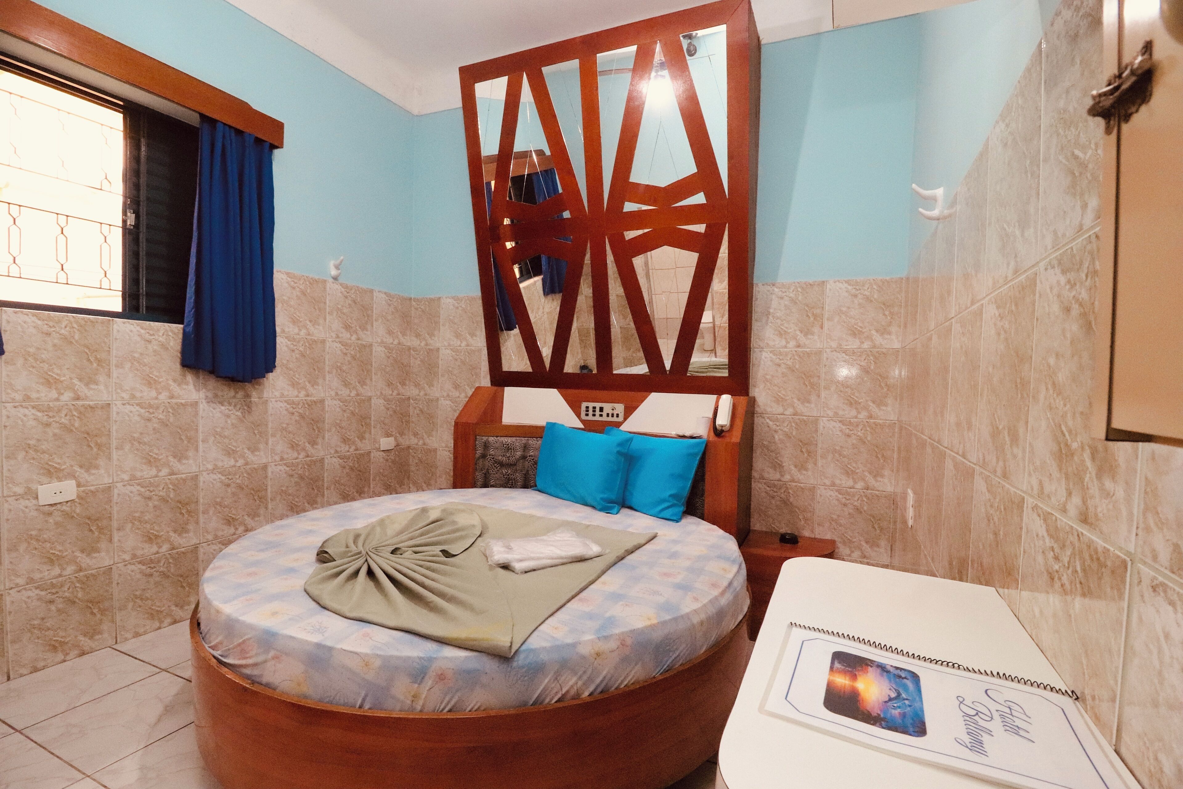A circular bed with a patterned mattress, a wooden headboard, and a blue pillow.