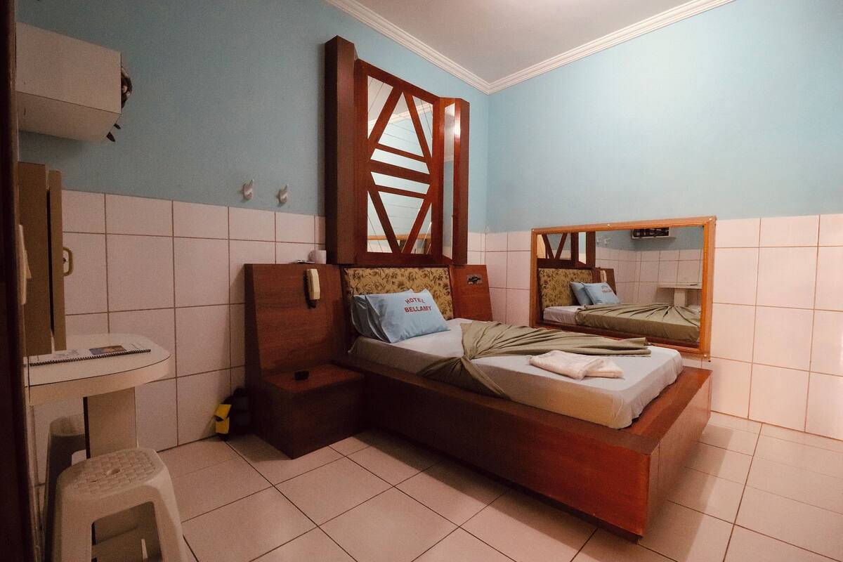 A bedroom with a bed, bedside tables, a mirror, and a small stool.