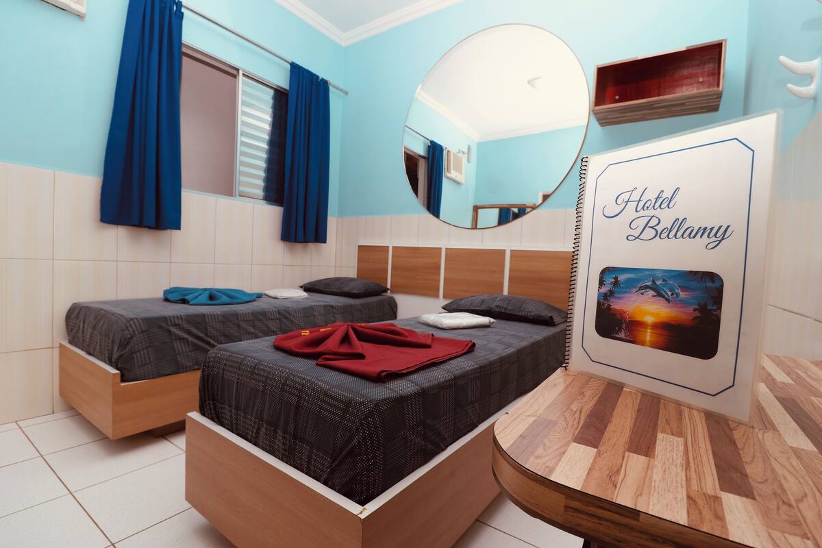 A hotel room with two beds, a mirror, a wooden headboard, a wall-mounted shelf, and a framed picture.