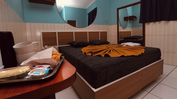 Una habitación de hotel con cama, mesita de noche con bandeja de aperitivos, espejo y estante en la pared.