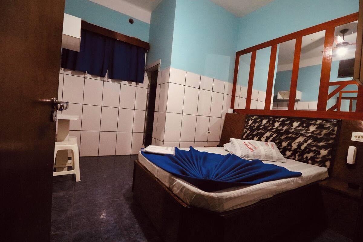 A bedroom with a bed, a wooden headboard, a mirror, a white stool, and a blue curtain.
