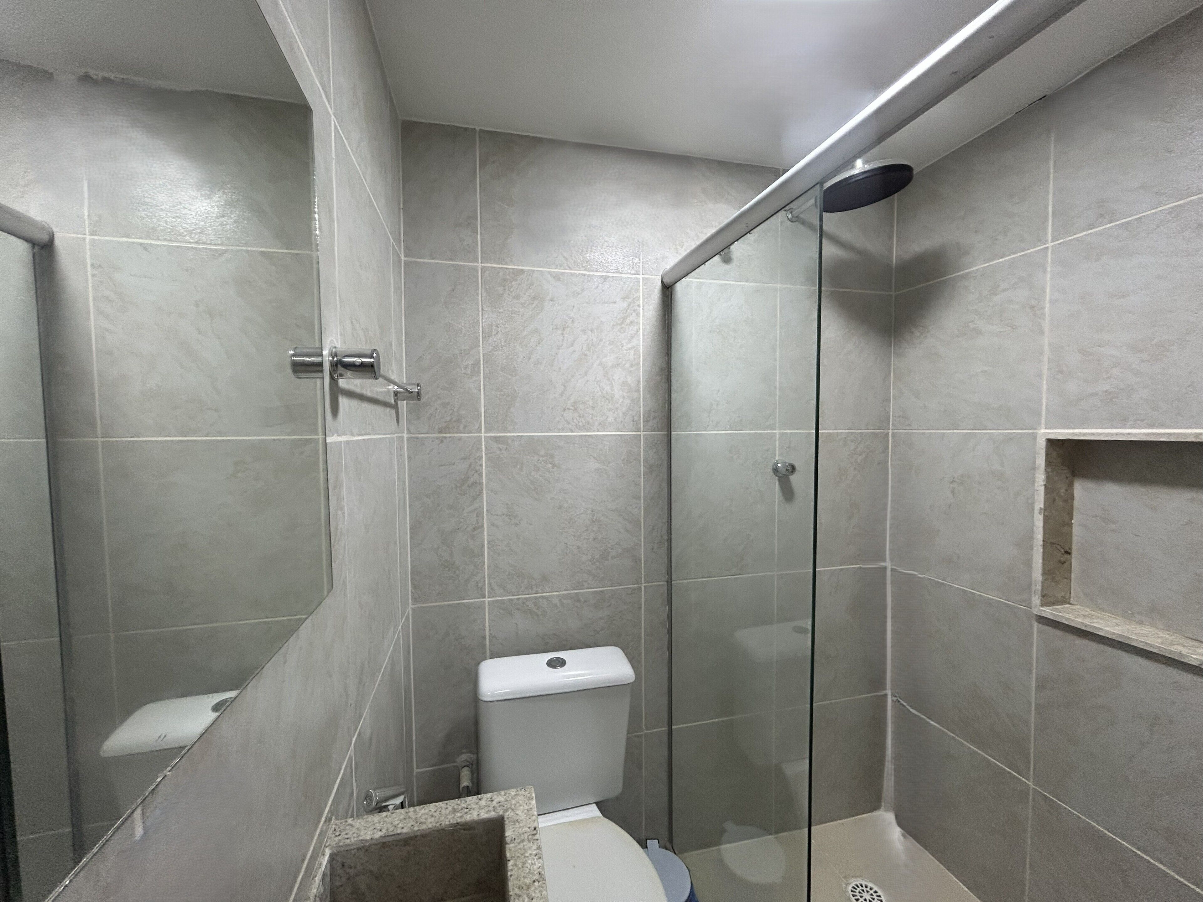 A shower area with a glass door, a toilet, and a small shelf.