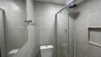 A shower area with a glass door, a toilet, and a small shelf.