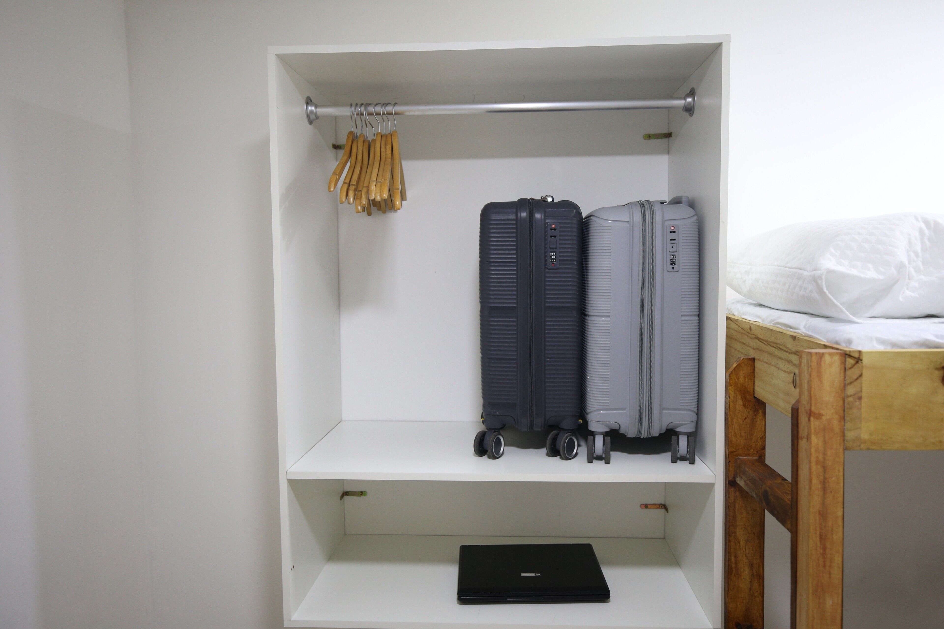 A white wardrobe with two suitcases and a laptop on the shelf.
