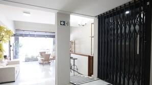 Vestíbulo de hotel con mostrador de recepción, una escalera y vista al área de estar exterior.