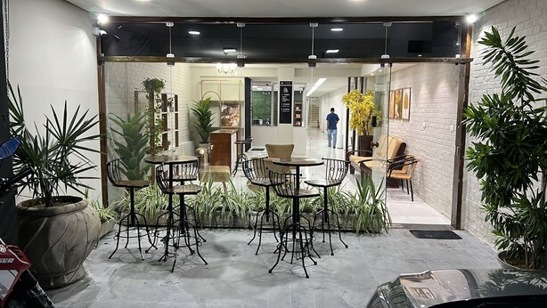 Un espacio interior moderno con mesas y sillas, plantas en macetas y una persona caminando al fondo.