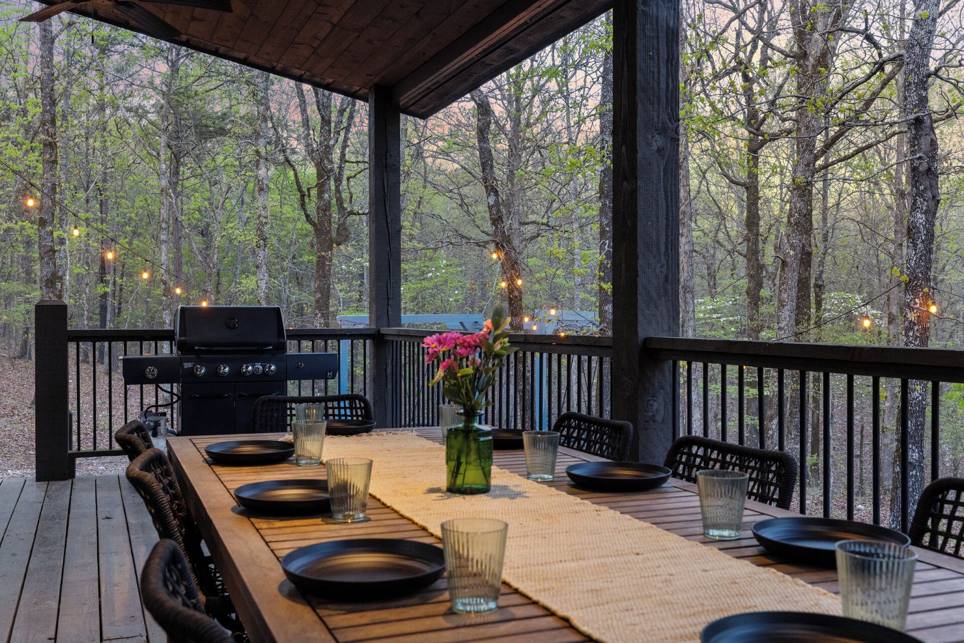 An outdoor dining area with a grill, tables, chairs, and string lights.
