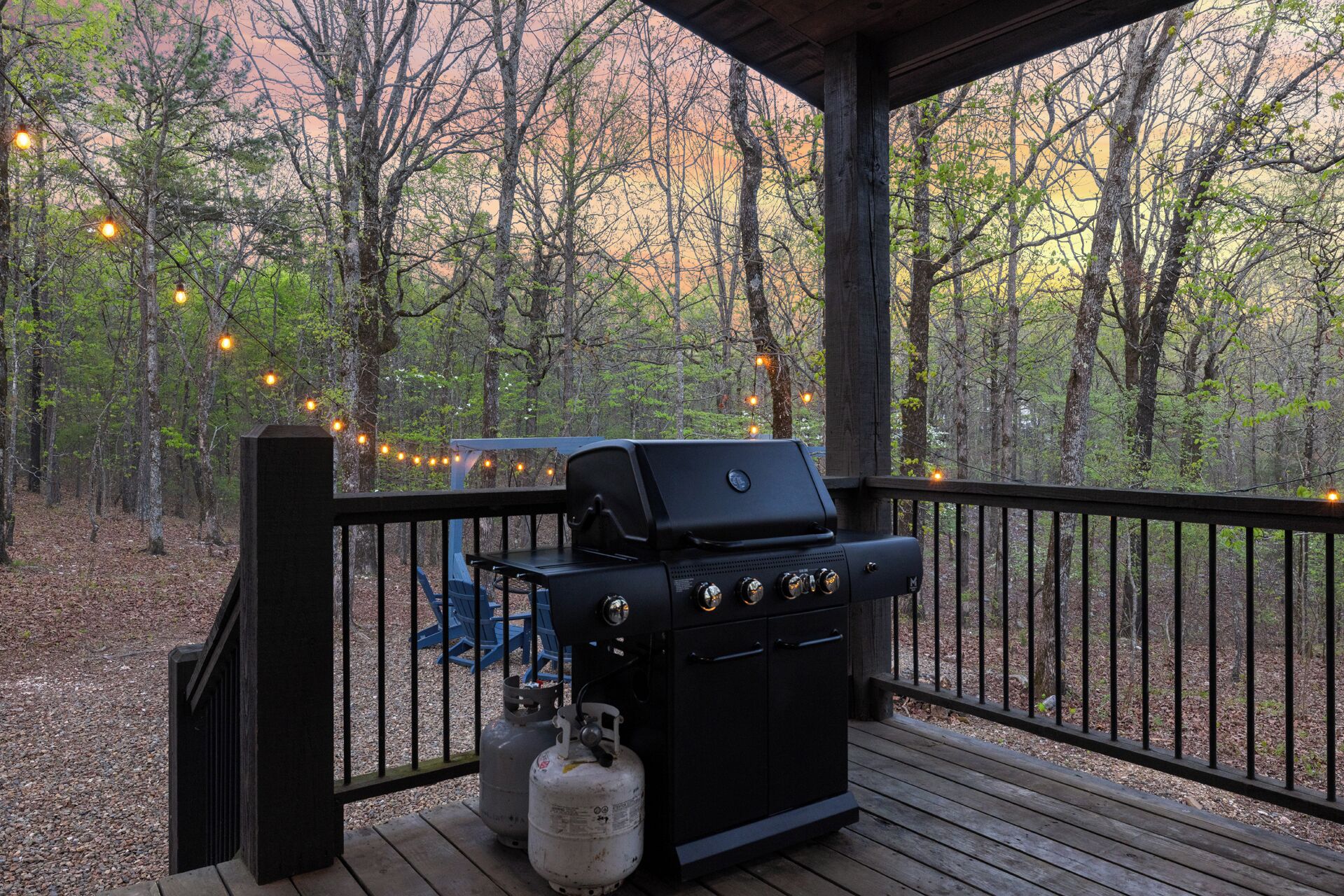 A barbecue grill on a wooden deck with a view of a forest.