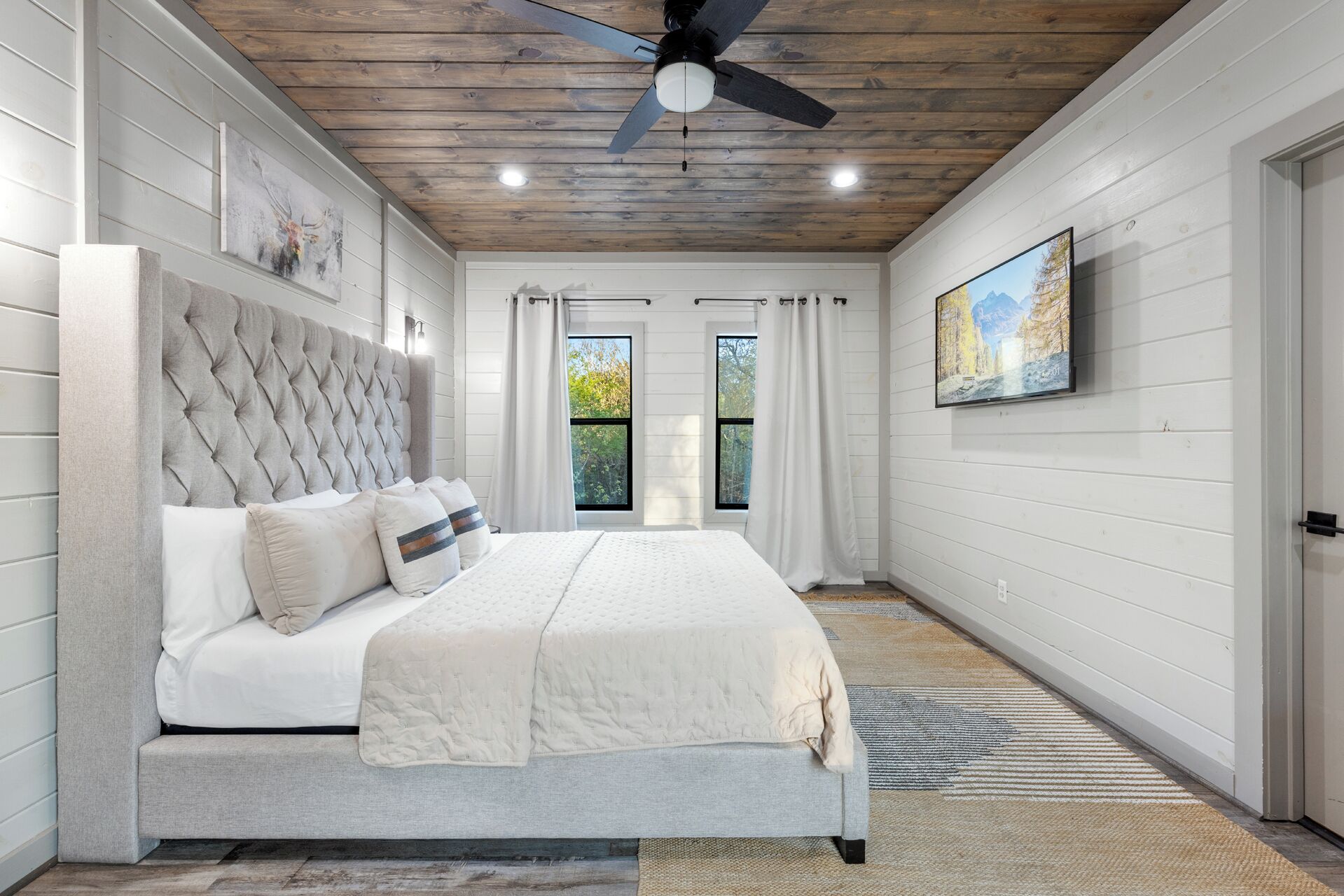 Een slaapkamer met een groot bed, een plafondventilator en een schilderij aan de muur.