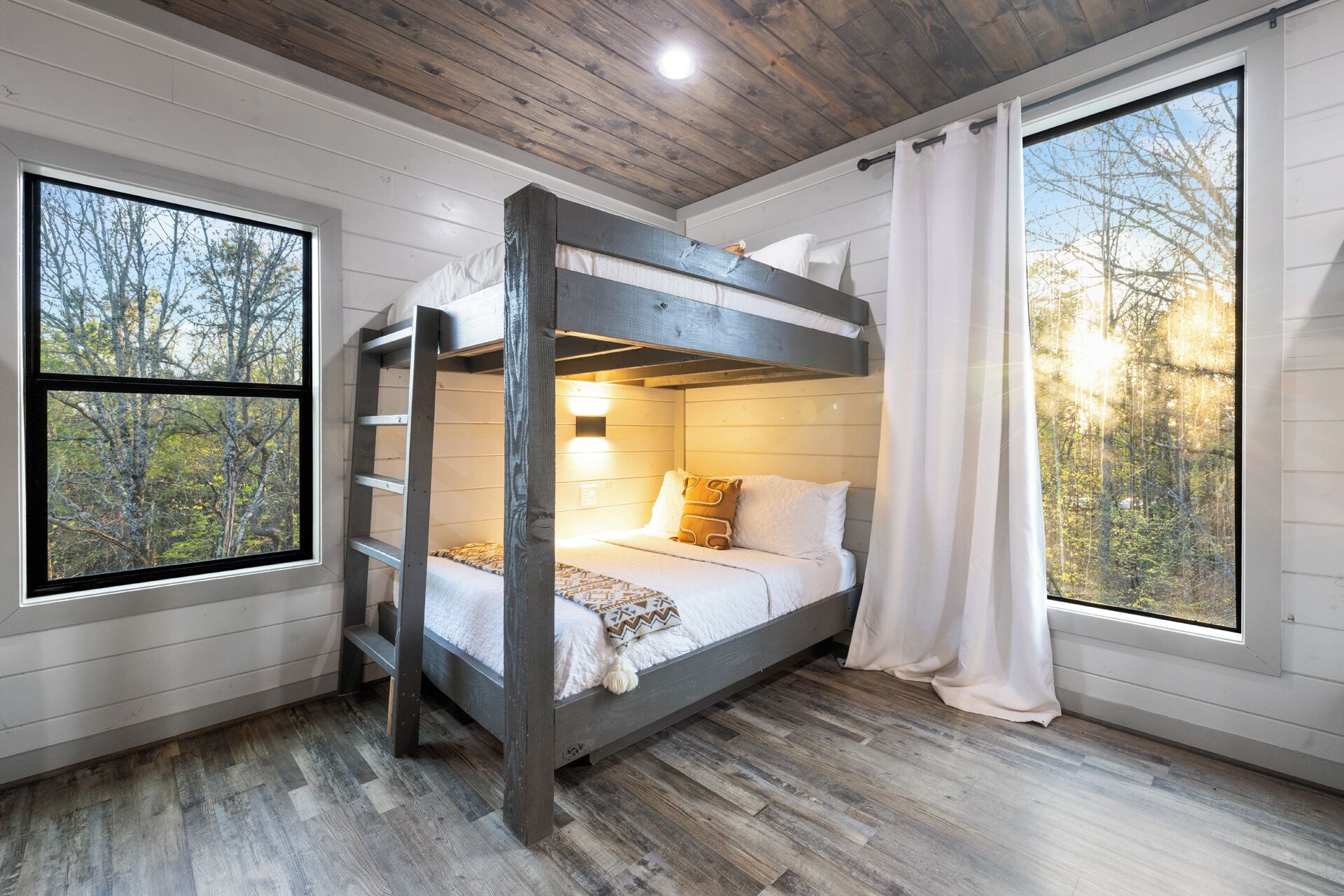 Habitación con literas, techo de madera, ventanas amplias y vista a los árboles.