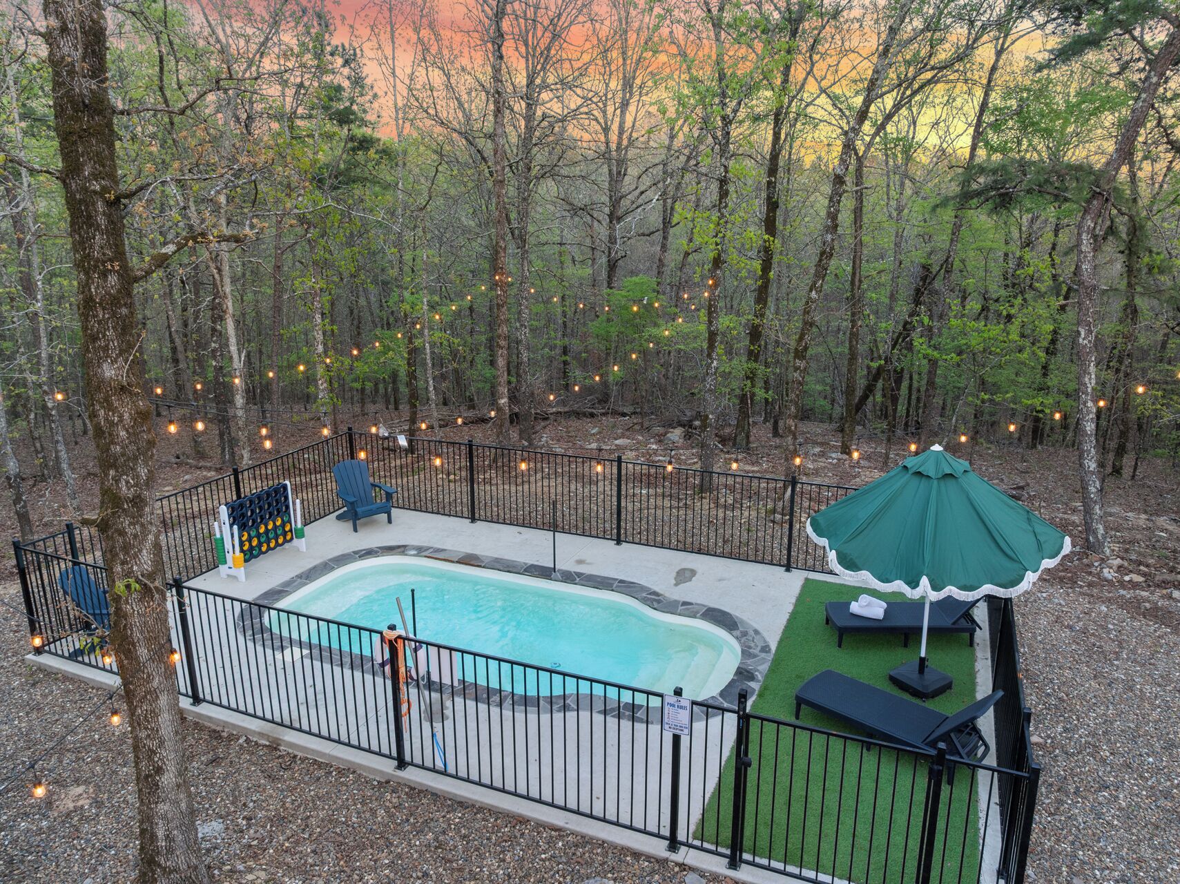 A backyard with a swimming pool, a deck, a green lawn, and a fence.