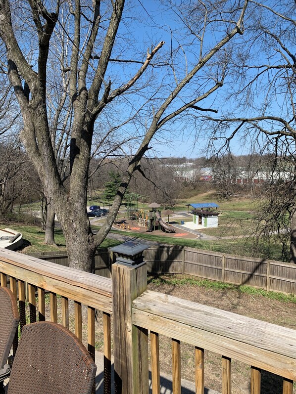 A wooden deck with a view of a playground and a fenced area.