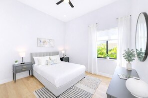 Ein modernes Schlafzimmer mit Bett, Nachttischen, Schreibtisch, Spiegel und einem Fenster mit Vorhängen.