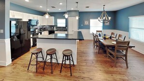 Een moderne keuken met een centraal eiland, barkrukken, een houten eettafel en stoelen.
