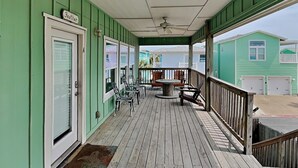 A covered porch with a table and chairs, a door labeled 'Feather,' and a view of a green building. - Fin & Feather | Spacious Port A Home, Steps to Sand (Port Aransas)