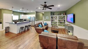 A modern living room with a brown leather sofa, a wooden coffee table, and a television on the wall. - Fin & Feather | Spacious Port A Home, Steps to Sand (Port Aransas)