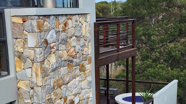 Un edificio moderno con fachada de piedra, terraza de madera y bañera de hidromasaje.