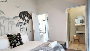 Un dormitorio con cama, un mural en la pared, y un baño con lavamanos y espejo.