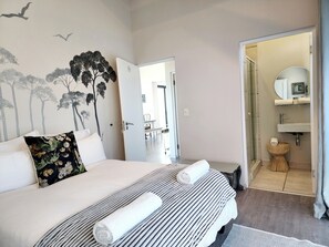 A bedroom with a bed, a wall mural, a bathroom with a sink and mirror. - Fabulous 5-bedroom house in serene Onrusrivier perfect for families and Friends (Onrusrivier)
