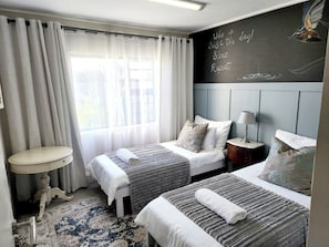 A hotel room with two beds, a small table, a lamp, and a chalkboard with motivational writing.