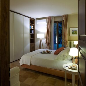 Un dormitorio con cama, mesita de noche, lámpara y vistas al exterior.